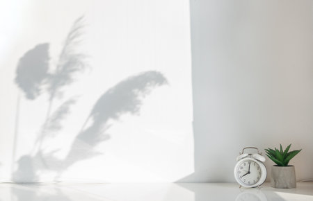 Front view of white table with alarm clock and house plant, copy space.の写真素材