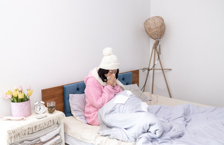 Sick Asian woman rubbing nose with tissue paper lying on bed at homeの写真素材