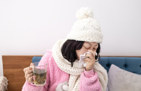 sick asian woman sneezing and holding a cup of teaの写真素材
