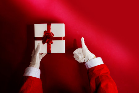 Santa Claus holding a gift box with red ribbon on a red backgroundの写真素材