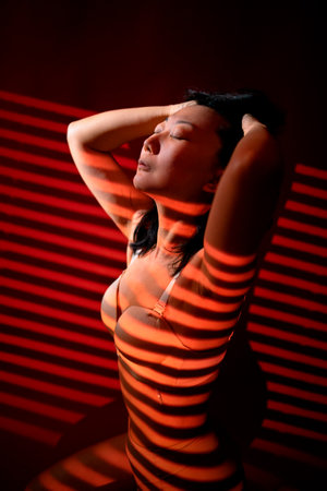 Beautiful young asian woman in underwear with blinds on a dark backgroundの写真素材