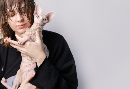 Young woman with a sphynx cat on a gray background