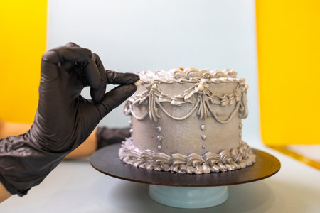 Female hands in black gloves decorate a cake with white cream.