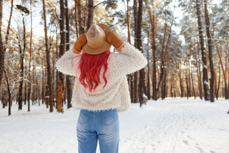 Happy young woman walking in forest among snow covered pine trees in winter day. Back view.の写真素材