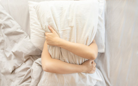 Too lazy to get out of bed, a woman covers her face with a pillow, top view.の写真素材