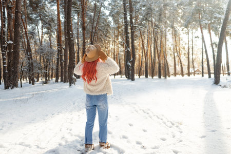 Back view of woman in warm winter clothes enjoying freedom while walking in snowy forest in cold weather.の写真素材
