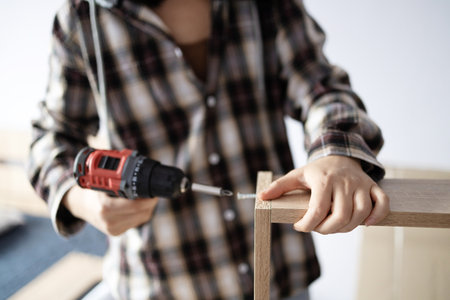 Woman screwing screws into a wooden plate to assemble a bedside table. DIY self-assembly with the help of a guide. Home design concept.の写真素材