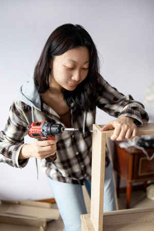 Young asian woman using drill to drill a wooden plank in the roomの写真素材
