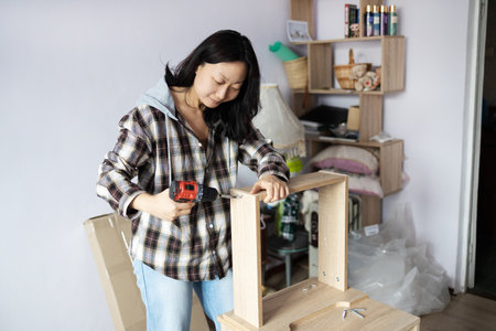 Young woman assembling furniture at home using a cordless screwdriver.の写真素材