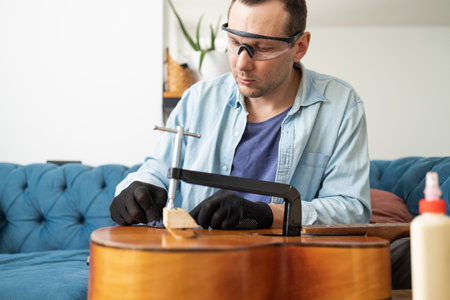 Man repairing acoustic guitar in his living room at home. He is wearing glasses.の写真素材
