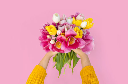 Female hands holding bouquet of tulips on pink background with copy space