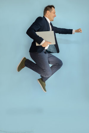 Full length photo of attractive young guy dressed classic formal suit running fast jumping empty space isolated color background.の写真素材