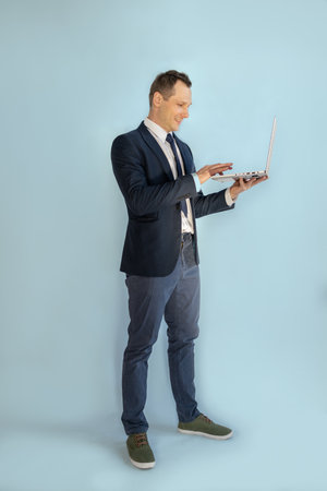 Full length portrait of a businessman using laptop on blue background.の写真素材
