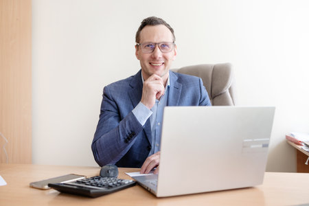 Portrait of a smiling businessman working with laptop at his office deskの写真素材