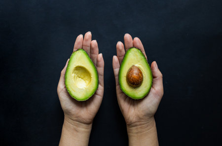 Avocado in female hands on a black background. Top view.