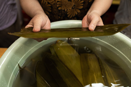 Woman's hand wrapping cake Zongzi or rice dumpling is glutinous rice with sweet or savory fillings wrapped in bamboo or reed leaves.の写真素材