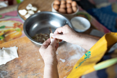 Chinese senior woman making Asian Chinese dumplings with meat or vegetable filling at home.