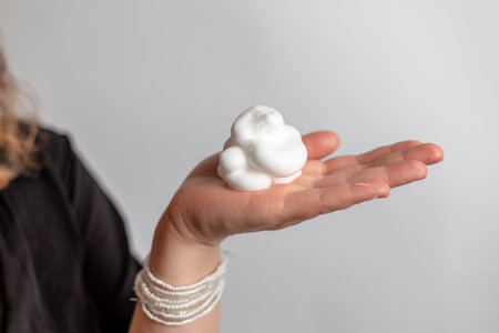 Close up of a woman's hand holding a white foam ball on a gray backgroundの写真素材