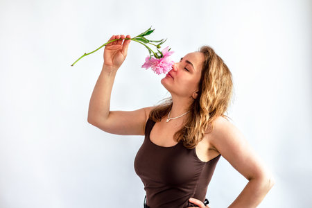 Young woman smelling a pink flower on a white background. Studio shot.の写真素材