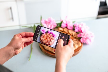 Woman taking a photo of homemade banana pie with mobile phone at homeの写真素材