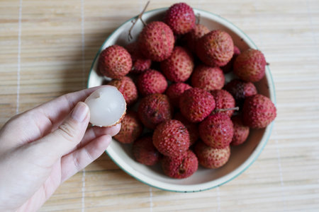 Hand taking fresh lychee fruit from plate, eating exotic fruit.の写真素材