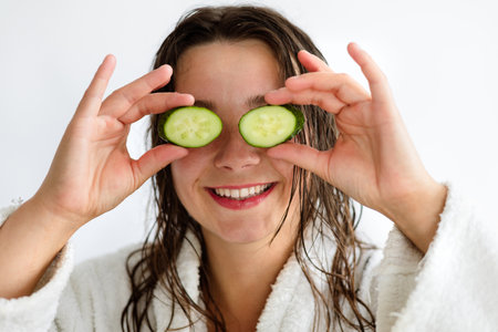 Young woman holding slices of cucumber in front of her eyes.の写真素材