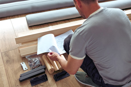 Young man assembling furniture at home, sitting on the floor and assembling furniture.の写真素材
