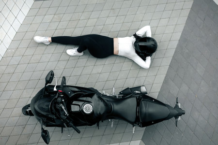 Top view of a girl lying on the ground next to her motorcycle