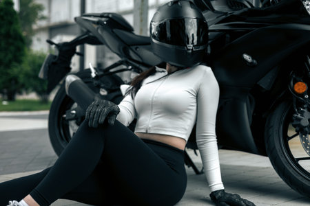 Biker girl in sportswear sitting on the road near her motorcycle