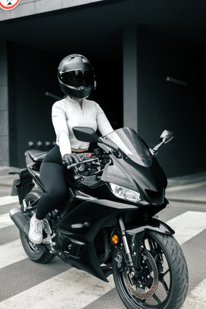 Beautiful young woman in a white blouse and black leather jacket riding a black motorbikeの写真素材