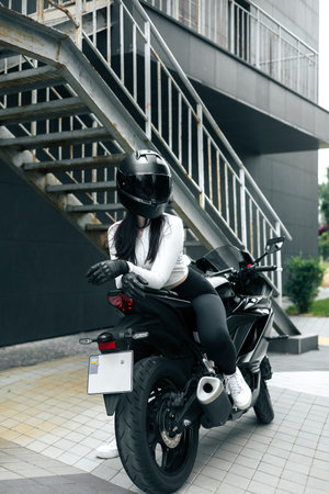 Biker Woman with Helmet posing on street. Cool competitive female motorcyclist wearing protective gearの写真素材
