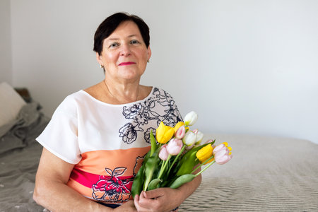 Elderly woman with a bouquet of tulips at homeの写真素材