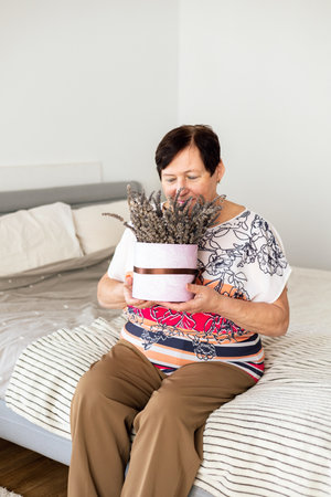Portrait of senior woman relaxing in bedroom with bunch of flowers in hug.の写真素材