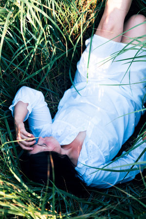 Field, sunshine and countryside with woman, flowers and smile with peace, sleeping and calming. girl laying on the grass, relax and beauty with nature, weekend breakの写真素材