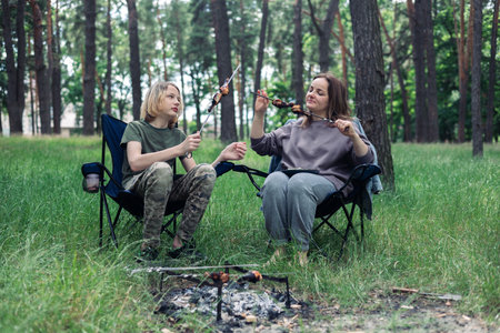 Mother and son camping in the forest, sitting on a folding chair. Camping, recreation, hiking.の写真素材