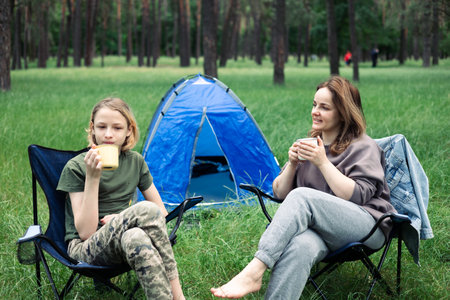 Mother and son camping in the forest, sitting on a folding chair. Camping, recreation, hiking.の写真素材