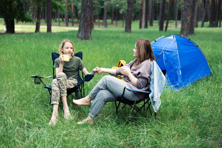 Mother and daughter camping in the forest, sitting on a folding chair.の写真素材