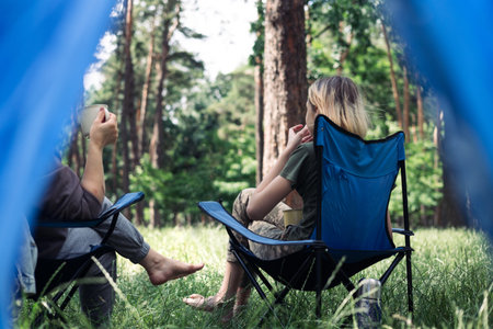 Mother and son camping in the forest, sitting on a folding chair. Camping, recreation, hiking.の写真素材