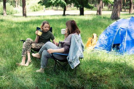 Mother and son sitting in camping chair and drinking tea in summer forestの写真素材