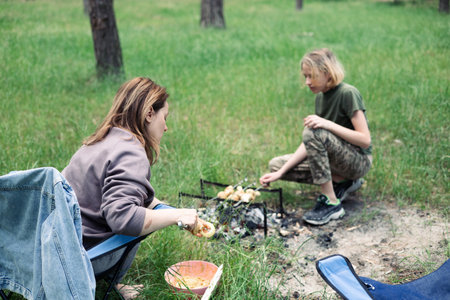 Young mother and son cooking sausages on campfire in summer forestの写真素材