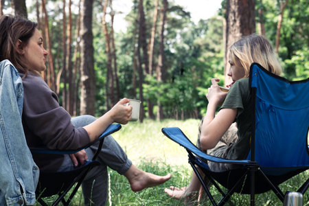 Mother and son camping in the forest, sitting on a folding chair. Camping, recreation, hiking.