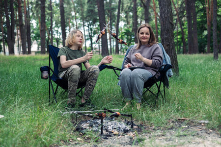 Happy family with teen boy on a picnic near the tent and grill a barbecue in a pine forest. Camping, recreation, hiking.の写真素材