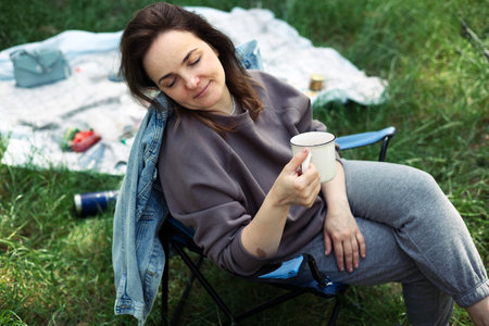 A young woman with a cup of coffee on a picnic in the parkの写真素材