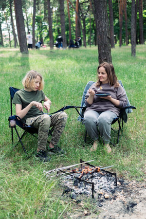 Happy family with teen boy on a picnic near the tent and grill a barbecue in a pine forest. Camping, recreation, hiking.の写真素材
