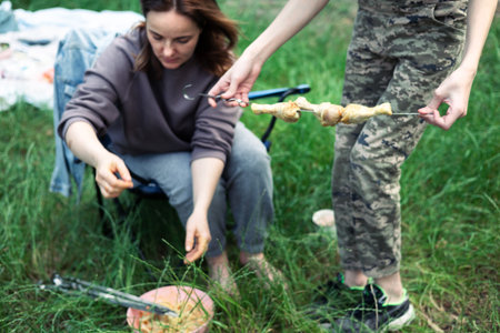 Young woman in camouflage cooking meat on skewer outdoors. Selective focus.の写真素材