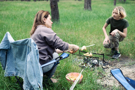 Happy family with teen boy on a picnic near the tent and grill a barbecue in a pine forest. Camping, recreation, hiking.の写真素材