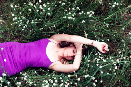 Relaxed girl posing with wild flower in green spring park outdoor. Girl on green grass background....