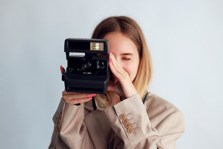 A young girl holding polaroid camera against a white background.