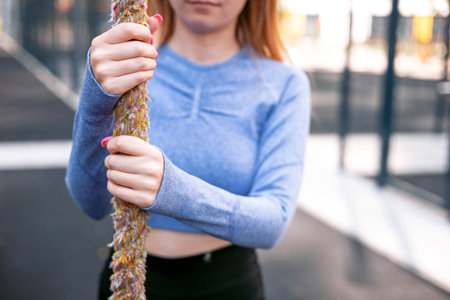 Young woman performing rope climbs in the sports ground. Crossfit and fitness.