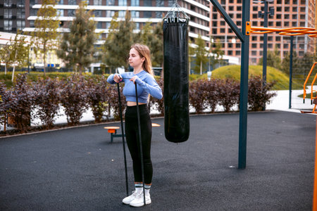 Woman training outdoors with resistance band, blonde girl in sportswear, in urban environment.